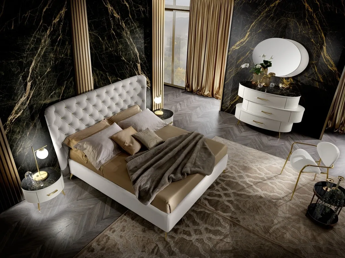 Modern bedroom featuring a white rounded bedside table with a black marble top and gold accents next to a tufted bed.